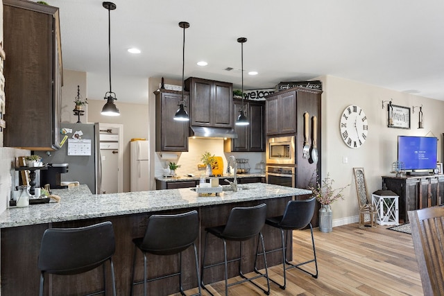 kitchen with under cabinet range hood, stainless steel appliances, a sink, dark brown cabinets, and light wood finished floors