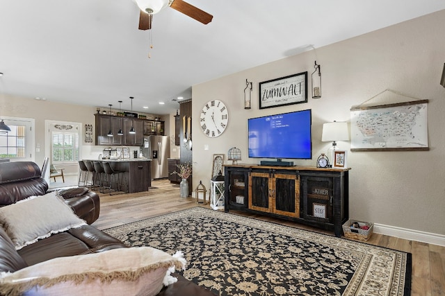 living area featuring ceiling fan, light wood-style flooring, and baseboards