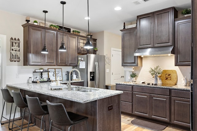 kitchen featuring light wood-style floors, a sink, a peninsula, stainless steel fridge, and under cabinet range hood