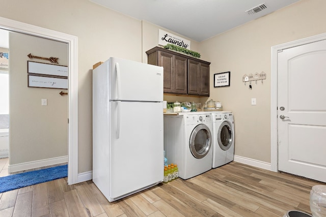 clothes washing area featuring separate washer and dryer, visible vents, baseboards, light wood-type flooring, and cabinet space