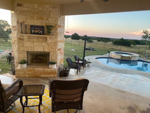 exterior space featuring a pool with connected hot tub, fence, an outdoor stone fireplace, and a rural view