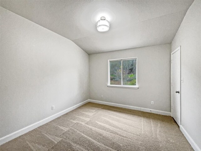 spare room featuring vaulted ceiling and carpet flooring