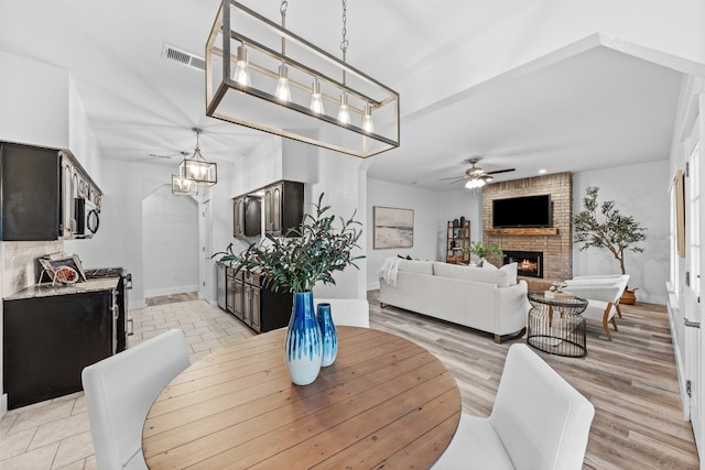 dining area with a fireplace, ceiling fan with notable chandelier, light hardwood / wood-style flooring, and brick wall