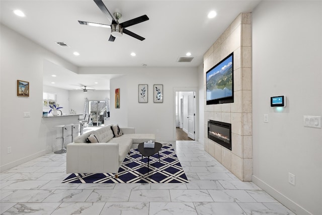 tiled living room with ceiling fan and a tiled fireplace