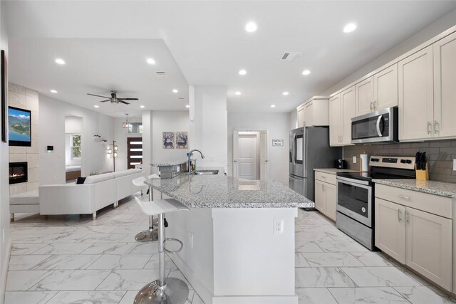 kitchen with stainless steel appliances, ceiling fan, light tile patterned floors, and a tile fireplace