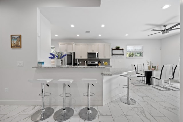 kitchen with appliances with stainless steel finishes, ceiling fan, light tile patterned floors, a breakfast bar area, and white cabinets