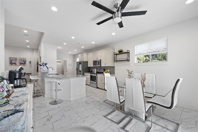 kitchen featuring ceiling fan, white cabinets, appliances with stainless steel finishes, light tile patterned floors, and a breakfast bar area