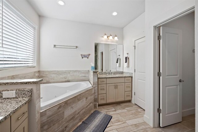 bathroom featuring tile patterned flooring, tiled tub, and vanity