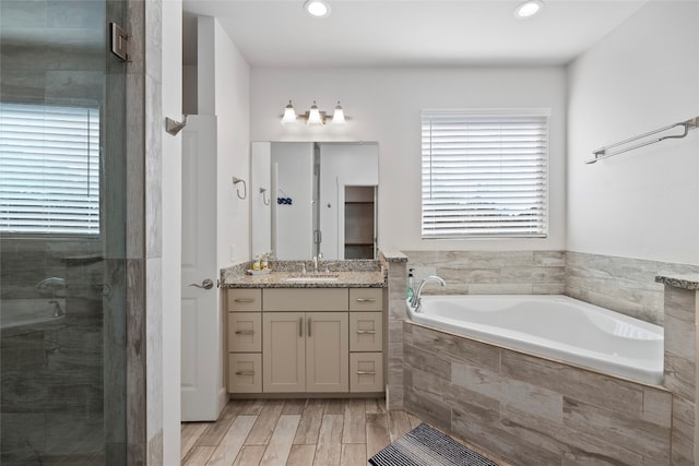 bathroom with a wealth of natural light, separate shower and tub, vanity, and wood-type flooring