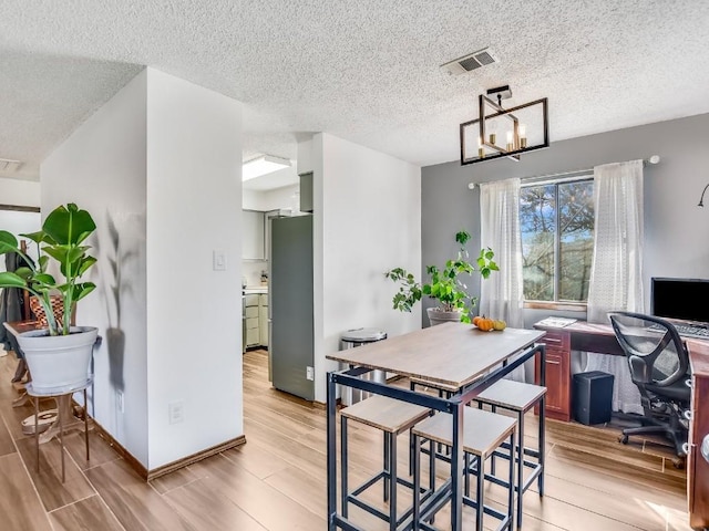 dining room featuring light wood-type flooring, a textured ceiling, and a chandelier