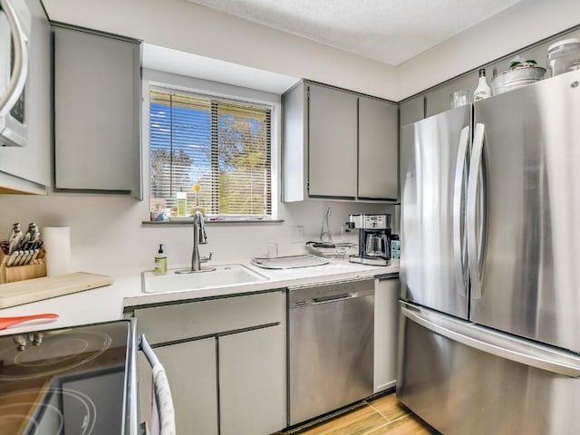 kitchen with a textured ceiling, gray cabinets, sink, and appliances with stainless steel finishes