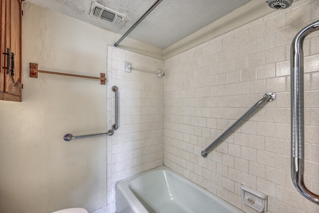 bathroom featuring a textured ceiling, toilet, and tiled shower / bath