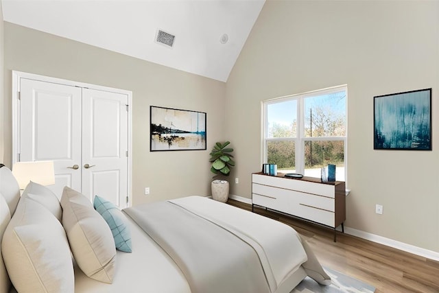 bedroom with wood-type flooring, high vaulted ceiling, and a closet