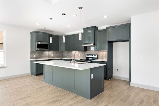 kitchen with pendant lighting, sink, an island with sink, appliances with stainless steel finishes, and light stone counters