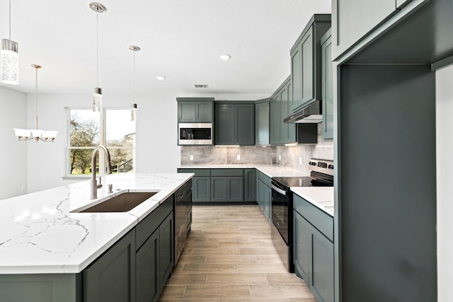 kitchen with light stone countertops, appliances with stainless steel finishes, backsplash, sink, and decorative light fixtures