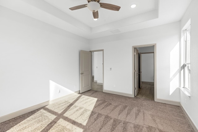 unfurnished bedroom with light carpet, a walk in closet, a raised ceiling, and ceiling fan