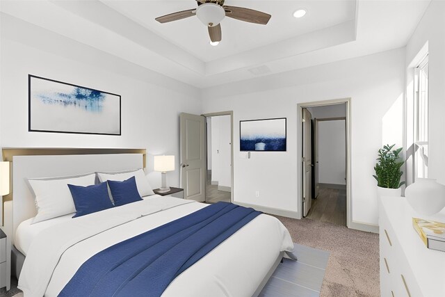 bedroom featuring ceiling fan, a raised ceiling, light colored carpet, and ensuite bath