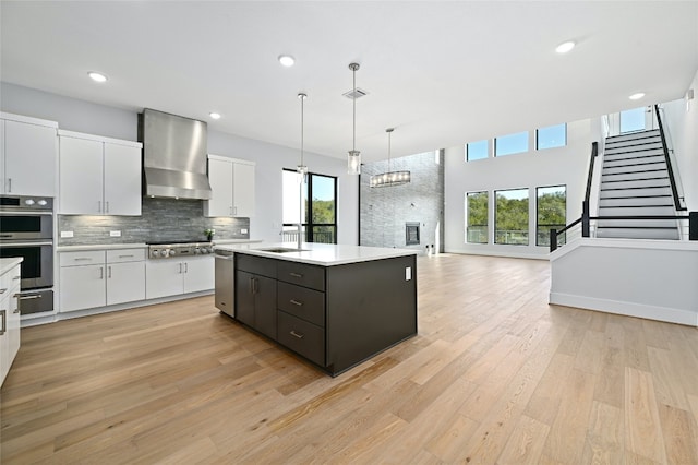 kitchen featuring white cabinetry, light wood-type flooring, plenty of natural light, and wall chimney exhaust hood