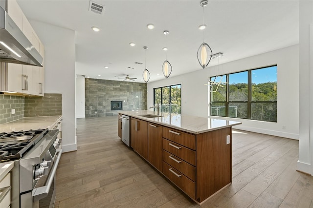 kitchen with light hardwood / wood-style flooring, white cabinets, wall chimney exhaust hood, a center island with sink, and tasteful backsplash