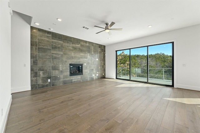 unfurnished living room with ceiling fan, a tiled fireplace, tile walls, and hardwood / wood-style floors