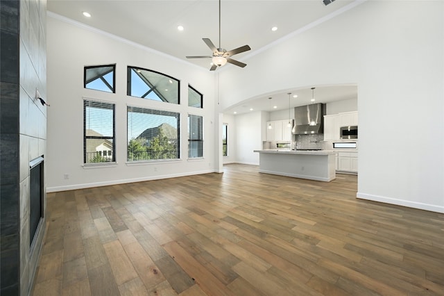 unfurnished living room with a large fireplace, high vaulted ceiling, crown molding, and hardwood / wood-style flooring