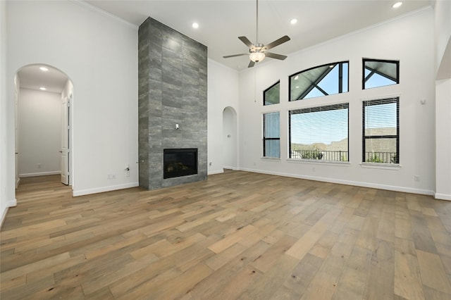 unfurnished living room featuring a tiled fireplace, high vaulted ceiling, light wood-type flooring, and tile walls