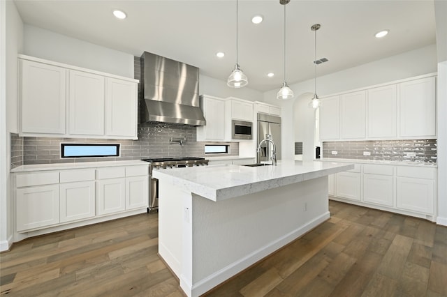 kitchen featuring built in appliances, backsplash, wall chimney range hood, and dark wood-type flooring