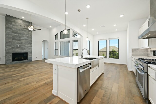 kitchen with an island with sink, stainless steel appliances, hardwood / wood-style flooring, and white cabinets