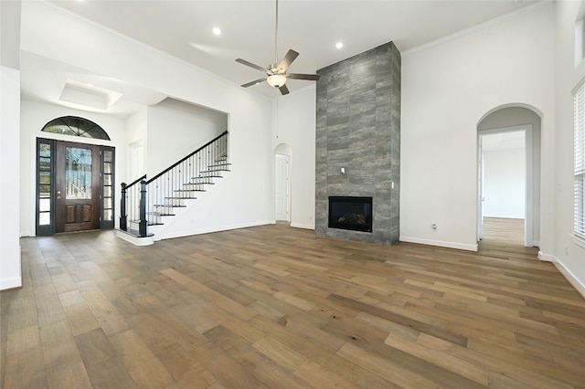 unfurnished living room with wood-type flooring, crown molding, a tiled fireplace, and ceiling fan