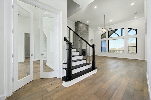 stairs with a towering ceiling, hardwood / wood-style flooring, crown molding, and ceiling fan