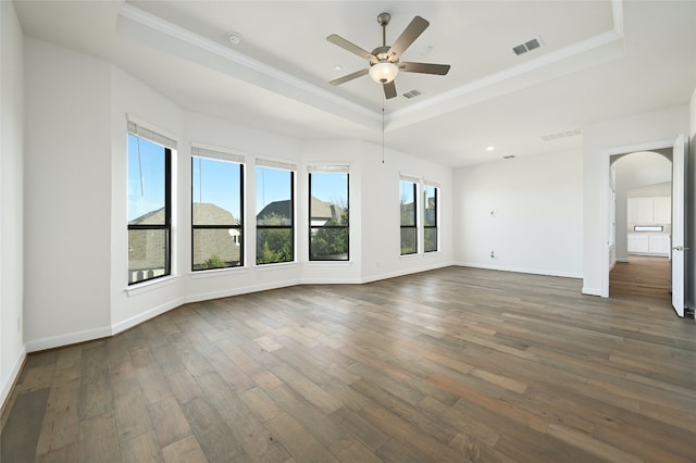 unfurnished living room with ceiling fan, dark wood-type flooring, a tray ceiling, and a wealth of natural light