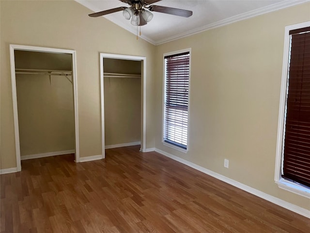 unfurnished bedroom featuring ceiling fan, dark wood-type flooring, vaulted ceiling, crown molding, and two closets