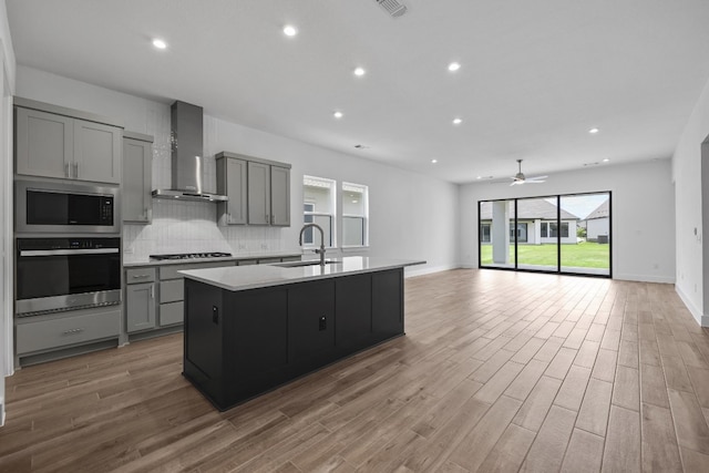 kitchen with wall chimney range hood, light hardwood / wood-style flooring, tasteful backsplash, sink, and stainless steel appliances