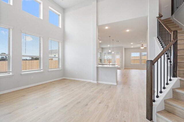 unfurnished living room featuring sink, a towering ceiling, ceiling fan, and light wood-type flooring