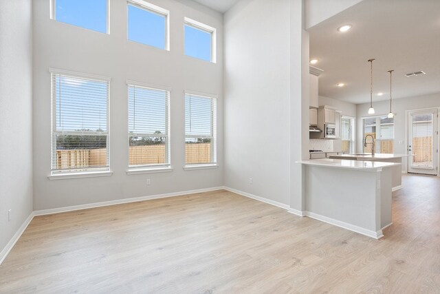 kitchen with stainless steel microwave, decorative light fixtures, white cabinetry, sink, and light hardwood / wood-style flooring