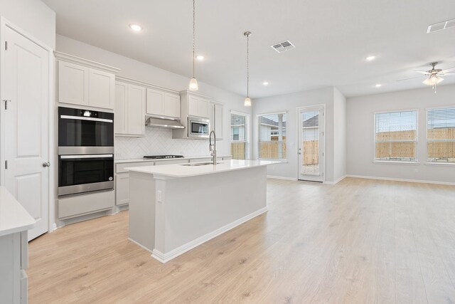 kitchen with appliances with stainless steel finishes, sink, a center island with sink, and white cabinets