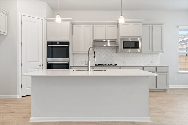 kitchen with pendant lighting, stainless steel appliances, light hardwood / wood-style floors, and a kitchen island with sink