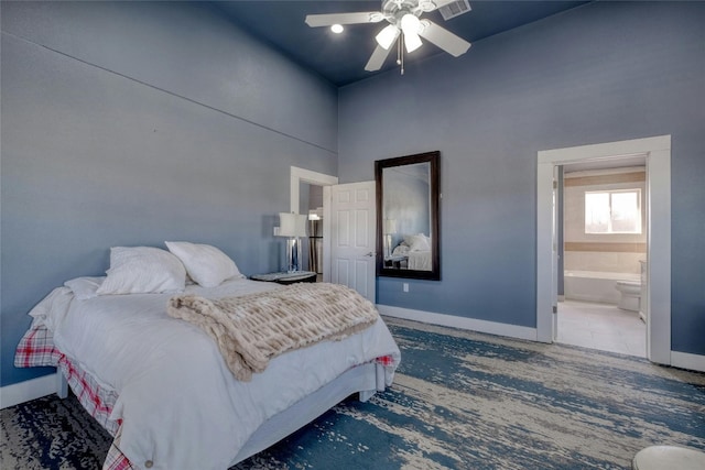 bedroom with dark tile floors, ceiling fan, connected bathroom, and a high ceiling