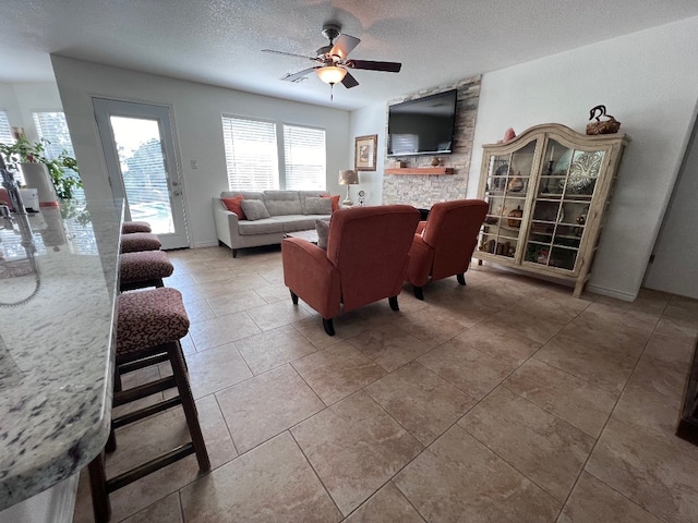 living room featuring light tile floors, ceiling fan, a textured ceiling, and a fireplace