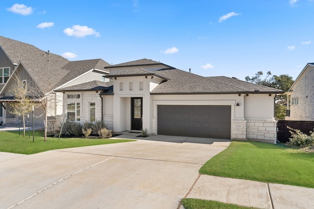 prairie-style house featuring driveway, a shingled roof, stone siding, an attached garage, and a front lawn