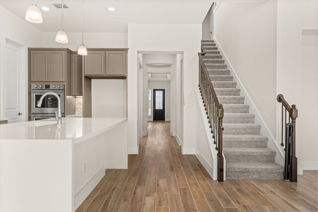 kitchen with hardwood / wood-style floors, pendant lighting, stainless steel double oven, and sink