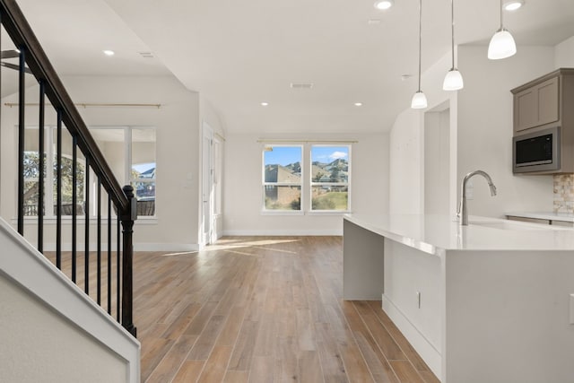 kitchen featuring hanging light fixtures, gray cabinets, light hardwood / wood-style flooring, and stainless steel microwave