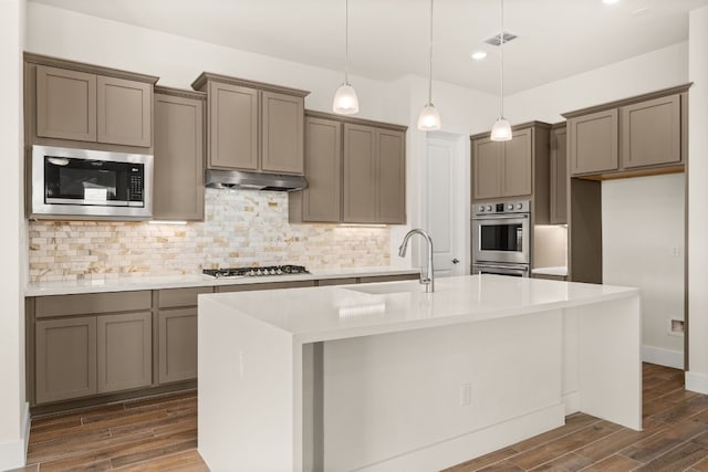 kitchen featuring a center island with sink, sink, hanging light fixtures, dark hardwood / wood-style flooring, and stainless steel appliances