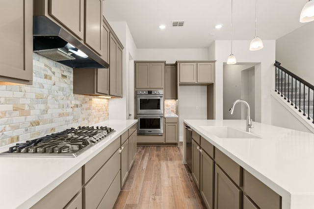 kitchen featuring stainless steel appliances, visible vents, light wood-style flooring, a sink, and under cabinet range hood