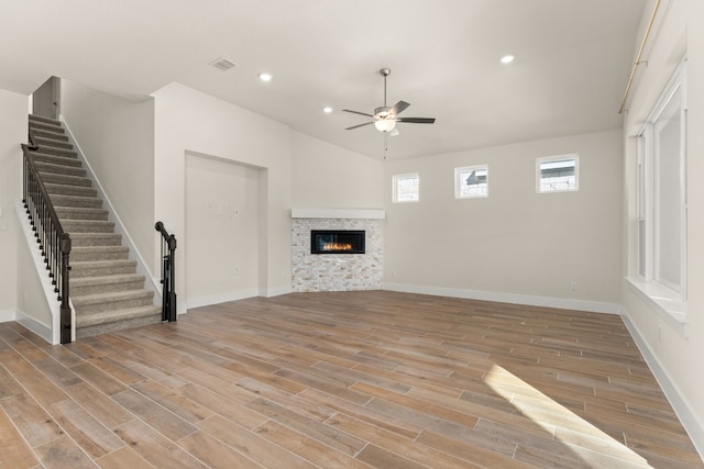 unfurnished living room with light wood-type flooring, a stone fireplace, and ceiling fan