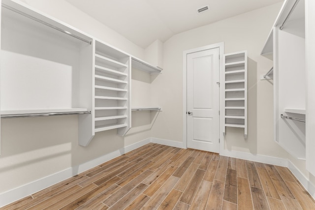 spacious closet with visible vents, vaulted ceiling, and wood finished floors