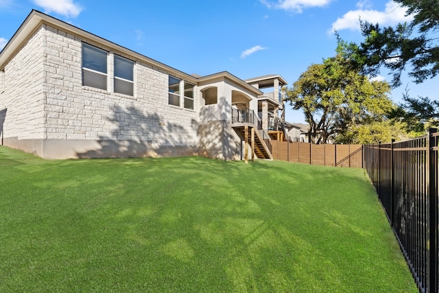 back of house featuring a fenced backyard, stairway, a lawn, and brick siding