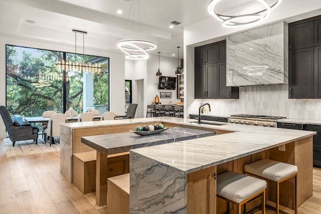 kitchen with sink, hanging light fixtures, light hardwood / wood-style flooring, a large island with sink, and a chandelier