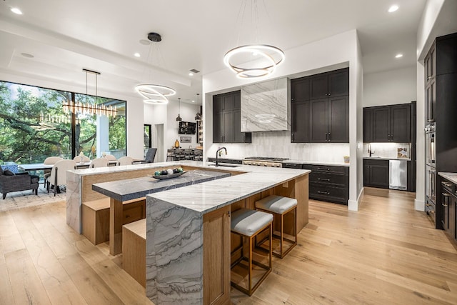 kitchen with a spacious island, sink, hanging light fixtures, light hardwood / wood-style flooring, and a notable chandelier