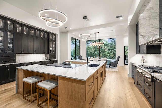 kitchen featuring sink, decorative light fixtures, a chandelier, stainless steel gas stovetop, and an island with sink